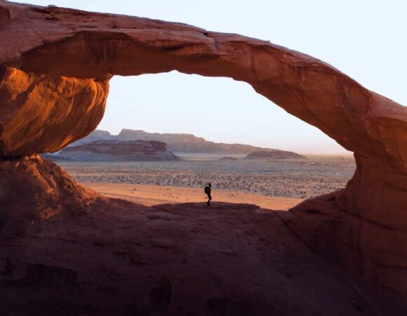 ROck bridge in Wadi Rum at sunset time with a person under it.