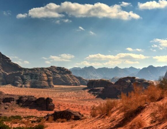 Red sand of the Wadi Rum desert under a blue sky with high mountains around.