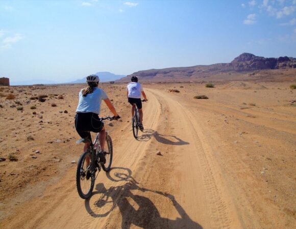 Two bikers along the Jordan bike trail from Petra to Wadi Rum ride on a sandy desert road