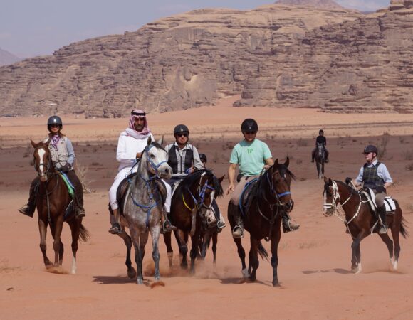 Group of horse riders trotting in the red Wadi Rum desert sand